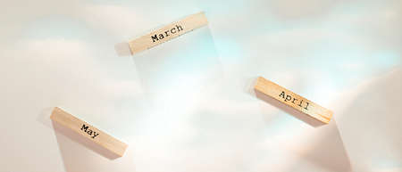 Three wooden blocks with names of spring months on white texture flooded with colorful lightの写真素材