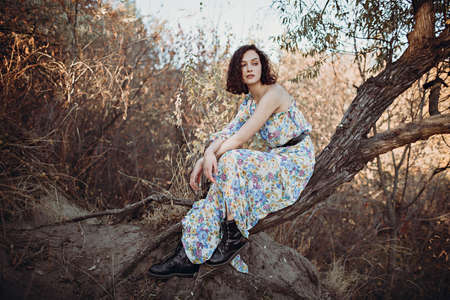 Young woman sits resting on leaning tree in autumn forest with her hands foldedの写真素材