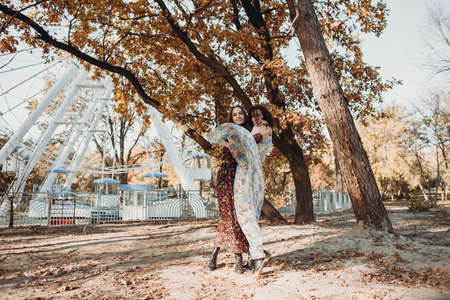 Two young women in vintage dresses having fun in park near ferris wheelの写真素材