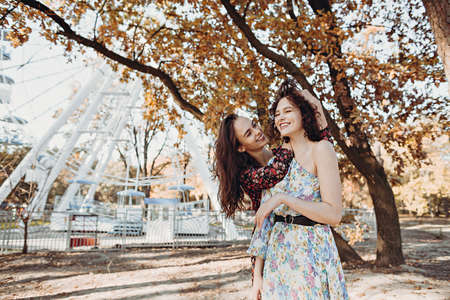 Two young women in vintage dresses having fun in park near ferris wheelの写真素材