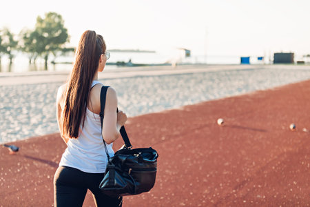 Young woman with sports bag walks on sports groundの写真素材