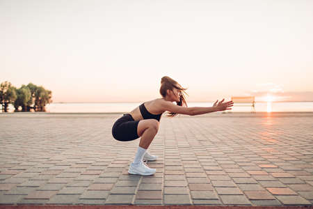 Young woman doing squats by the river at sunriseの写真素材