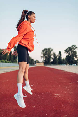 Young woman doing warm-up exercises on sportsground early in the morningの写真素材