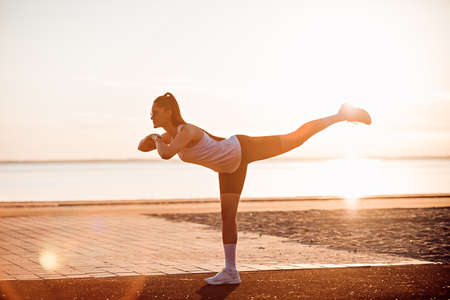 Young woman doing warm-up and stretching exercises on sportsground early in the morningの写真素材