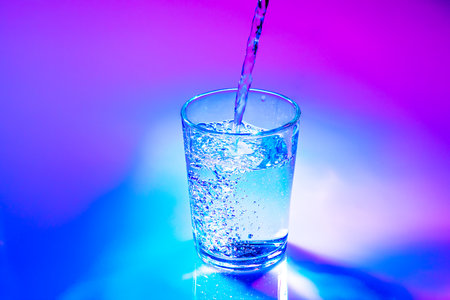 Water pouring into glass. Neon lights color aestheticsの写真素材