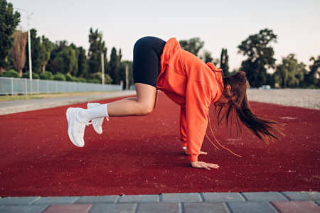 Young woman doing warm-up exercises on sportsground early in the morningの写真素材