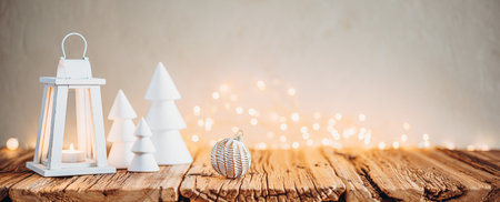 White Christmas trees, candle lantern and bokeh lights on wooden table in cozy atmosphereの写真素材