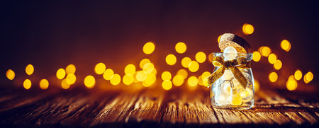 Small glass jar with Christmas lights on wooden planksの写真素材