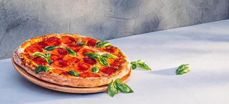 Pepperoni pizza with basil on kitchen table in sunlightの写真素材