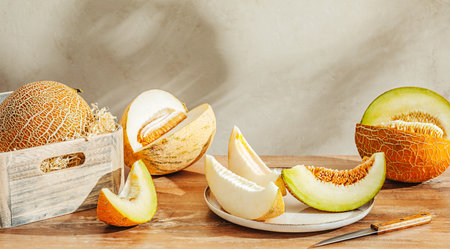 Various sliced melons on wooden table by stone wallの写真素材