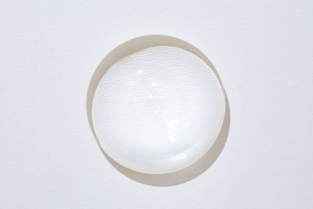 Clear circular glass lens resting on a textured white paper.の写真素材