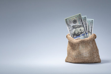A burlap bag brimming with hundred dollar bills highlights themes of wealth and abundance. The neutral background emphasizes the focus on financial success and investment opportunities.の写真素材