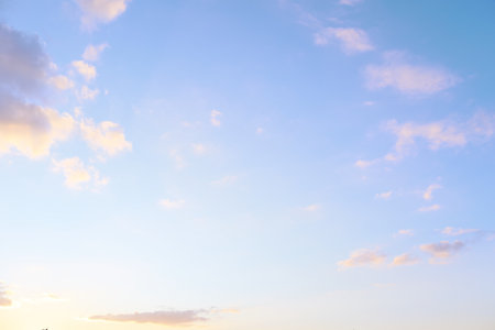 Soft colors blend in the sky as the sun sets, illuminating fluffy clouds framing tranquil evening atmosphere above a distant horizon.の写真素材
