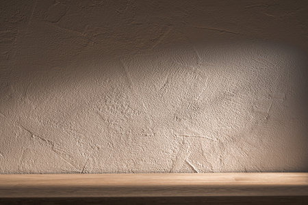 Soft lighting casts shadows on a textured wall, highlighting its details. A rustic wooden shelf sits underneath, creating cozy indoor space.の写真素材