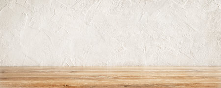 Rustic wooden table surface with a textured white wall background in a well-lit kitchen.の写真素材