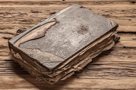 Old book resting on a weathered wooden surface with faded cover and worn pages revealing its history and significance.の写真素材