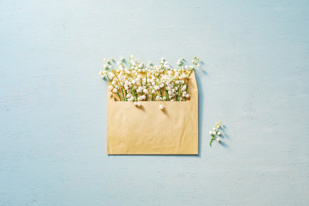 Lilies of the valley clustered inside a postal envelope on blue wooden surface.の写真素材