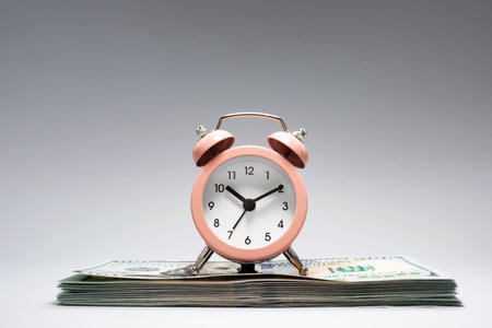 A pink alarm clock sits atop a tidy stack of cash, illustrating the connection between time management and financial planning during a calm and organized setting.の写真素材