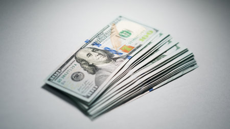 A close view of a stack of hundred dollar bills positioned on a neutral background.の写真素材