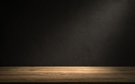 Empty wooden table in a dark room with textured wall background and soft lighting highlighting the surface.の写真素材