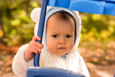 Beautiful baby girl in white jacket looking into the blue bike frame against autumn natureの写真素材