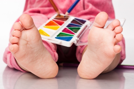 Baby's feet with paint and pencils isolated on whiteの写真素材