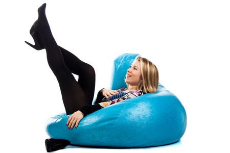 Portrait of a beautiful young girl sitting on a bean bag with her legs raised up isolated on white の写真素材