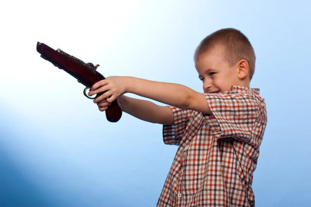 Cute boy playing with the gun against blue backgroundの写真素材