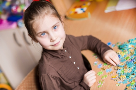 Cute little girl playing puzzles at the tableの写真素材