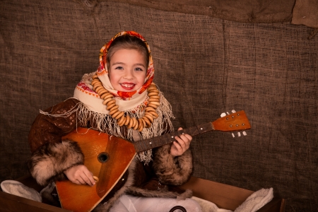 Beautiful russian girl in a shawl  sitting in a cart playing balalaikaの写真素材
