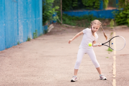 Adorable little child playing tennis with racket and a ball on tennis courtの写真素材
