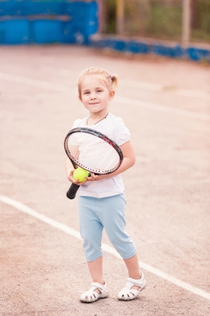 Adorable little child playing tennis with racket and a ball on tennis courtの写真素材