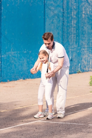 Instructor teaching a child how to play tennis on a court outdoorの写真素材