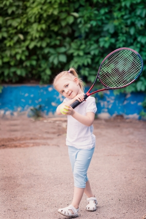 Adorable little child playing tennis with racket and a ball on tennis courtの写真素材
