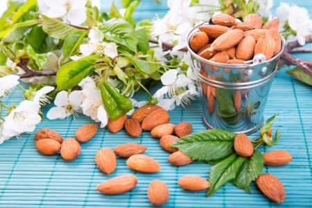 Almonds in a backet scattered over blue bamboo overlay with blooming flowers on backgroundの写真素材