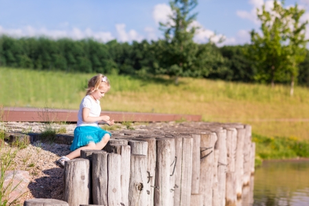 Cute little girl sitting near the lake in summertime in natureの写真素材