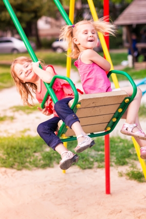 Beautiful little girl on a swings outdoor in the playground at summertimeの写真素材