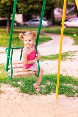 Beautiful little girl on a swings outdoor in the playground at summertimeの写真素材