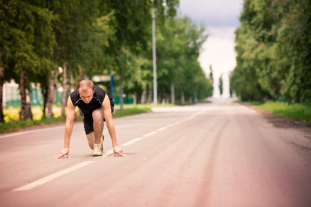 Sportive young man in starting position prepared to run on road