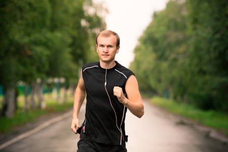 Sportive young man runner jogging at great speed on a roadの写真素材