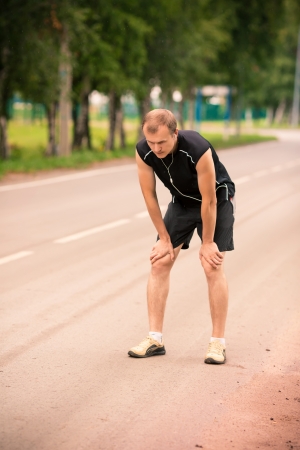 Sportive young man runner having rest after jogging on a roadの写真素材