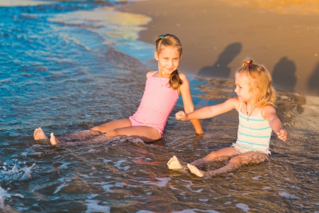 Two happy adorable kids playing in the sea on a beachの写真素材