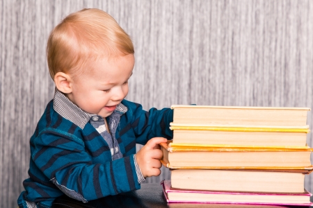 Adorable curious baby boy studying a pile of books indoorの写真素材