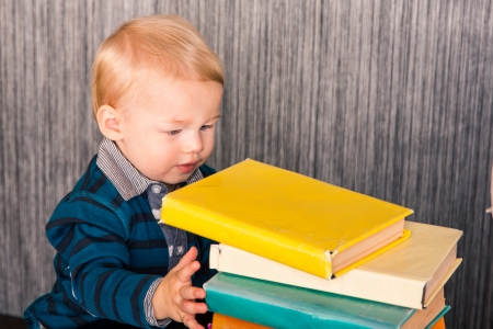 Adorable curious baby boy studying a pile of books indoorの写真素材