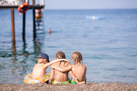 Backs of three children sitting on a beachの写真素材
