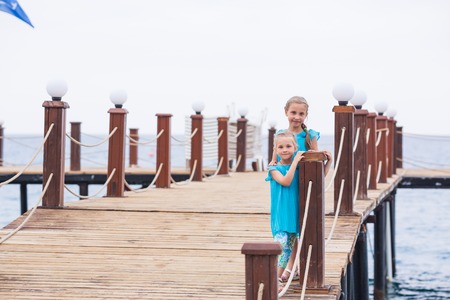 Portrait of beautiful little girls, sisters on the pier at the seasideの写真素材