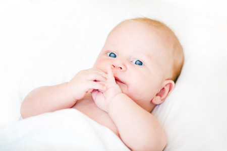 Peaceful newborn baby lying on a bed smiling on white sheetsの写真素材
