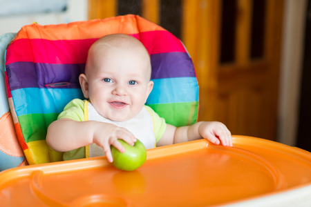 Adorable baby eating apple in high chairの写真素材