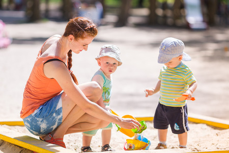 Mother playing helping two baby boys playing with sand in a sandboxの写真素材