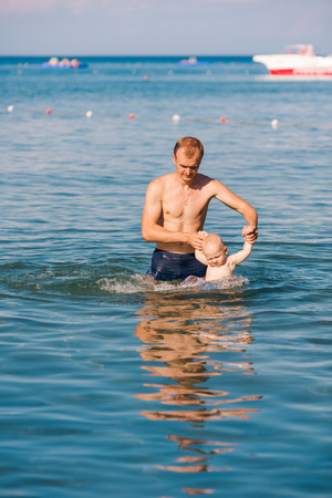 Happy father and baby having fun in the sea, exercising in whaterの写真素材